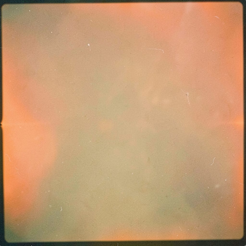 Fotografia analogica granulosa di un cavo di rete arancione avvolto su sfondo scuro, con luci soffuse e atmosfera casalinga da postazione internet